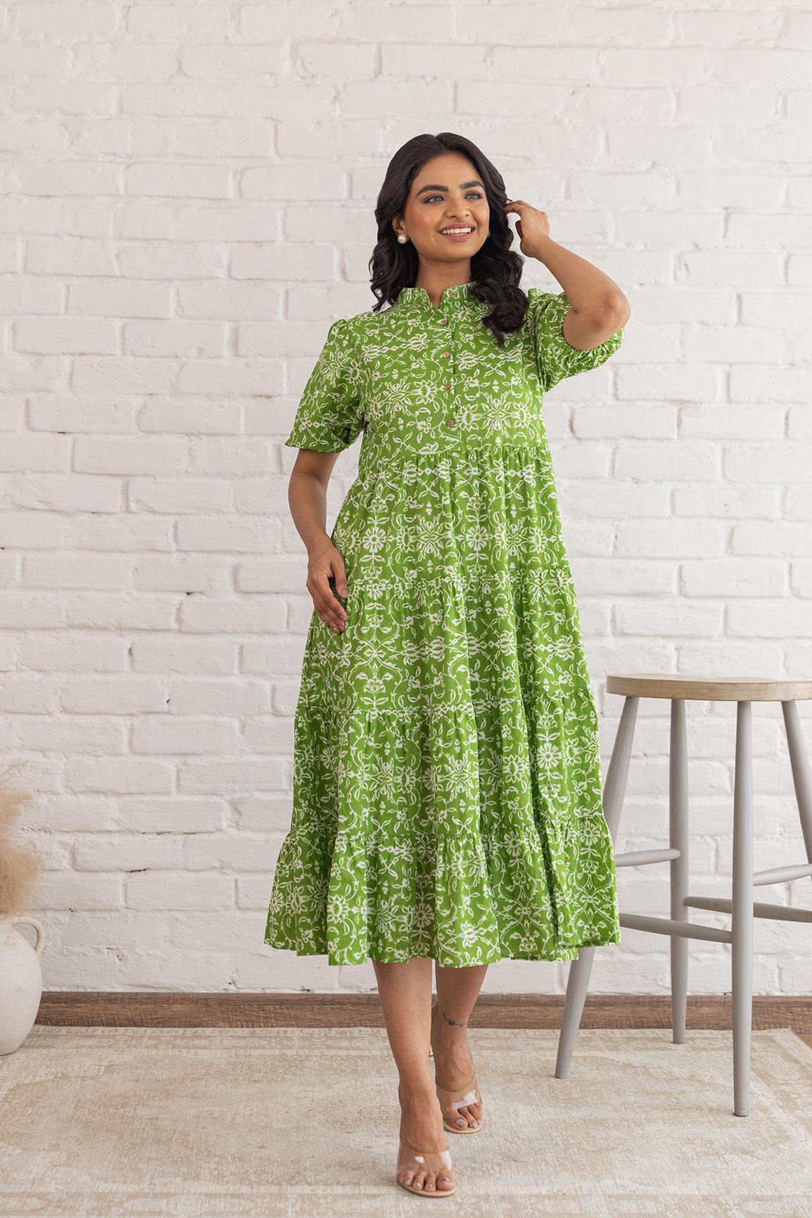 Woman in a green cotton maxi dress against a white brick wall.